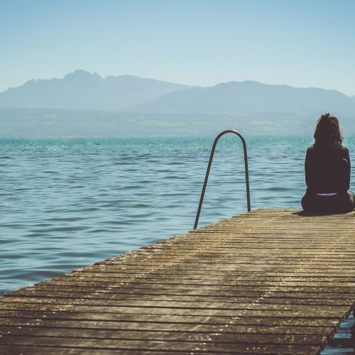 vrouw zit op een steiger aan het water
